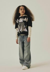 Svart grafisk t-shirt med leopardmönster och texten "Def Leppard" över en ljus långärmad tröja. Löst sittande ljusblå jeans och vita sneakers.