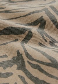 Tan fabric with a black tiger stripe pattern, displaying a textured surface with soft ripples and folds.