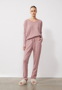 Vaffelstickad lounge-set i mjuk rosa, med en avslappnad V-ringad topp och byxor med dragsko och fickor. Mjuka, plyschiga tofflor fulländar looken.