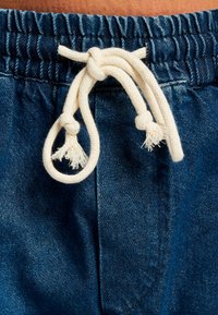 Pantalones cortos de mezclilla con una cintura elástica y un cordón blanco con extremos deshilachados, que exhiben un rico color azul y una sutil textura.