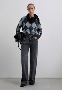 Pull en argyle gris avec accents noirs, jean large taille haute gris foncé, sac à main noir et foulard noir texturé.