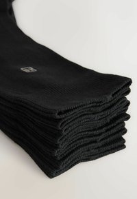 Calze di cotone nere impilate ordinatamente, con una texture a coste e un piccolo logo incorporato vicino al polsino, caratterizzate da un colore e un design uniformi.