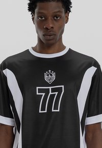 Jersey desportivo preto com detalhes em branco, apresentando um grande número "77" em branco e um logo no peito. Mangas curtas e design de gola redonda.