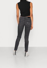 Svart ribbat ärmlöst linne, mörkgrå skinny jeans och vita högtoppsskor med svarta prickar, sett bakifrån.