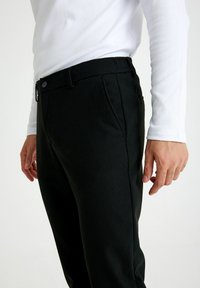 Zwarte broek van een gestructureerde stof, met een knoopsluiting, zijzakken en een slim fit ontwerp, gecombineerd met een wit overhemd met lange mouwen.