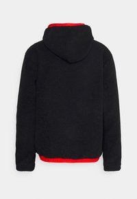 Schwarze Fleecejacke mit strukturiertem Finish, ausgestattet mit einer Kapuze und einem kontrastierenden roten Rippbund. Glatter Stoff, lässiger Schnitt.