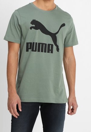 T-shirt vert en coton à manches courtes avec un logo Puma noir et une silhouette. Texture lisse avec un col rond et une coupe régulière.