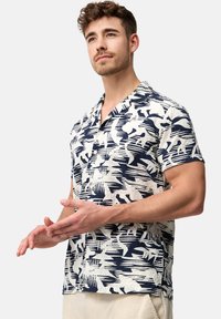 Camisa de manga corta en color crema con patrón abstracto en azul marino, diseño con cuello, ajuste relajado y tejido texturizado. Detalle de costura en el dobladillo.