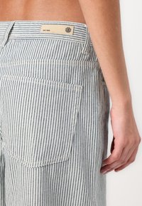 Gestreepte denim shorts in lichtblauw en wit, met een achterzak en een merklabel nabij de tailleband. Geweven stof met verticale lijnen.