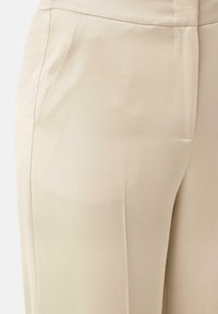 Beige broek gemaakt van een gladde stof, met zijzakken, een getailleerde pasvorm en subtiele plooien voor extra dimensie.