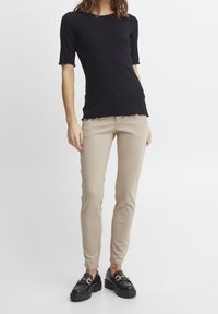 Black short-sleeve top with scalloped edges, paired with fitted beige pants and black platform loafers. Simple, smooth textures.