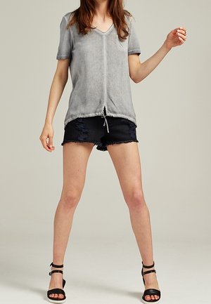 Gray short-sleeve V-neck top with a pocket, paired with distressed black denim shorts and black strappy sandals. Casual and relaxed fit.