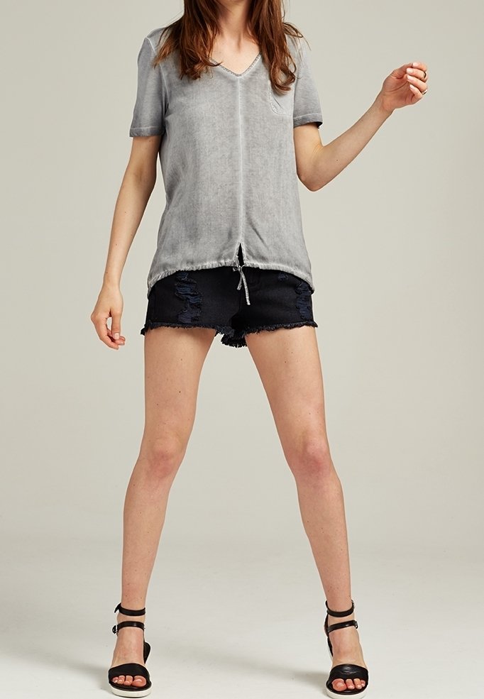 Haut gris à manches courtes en V avec une poche, associé à un short en denim noir déchiré et des sandales noires à lanières. Look décontracté et ample.