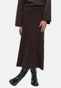 Ruskea neulepitsihame, jossa on istuva vyötärö, kapeneva siluetti ja teksturoitu kangas, yhdistettynä mustiin polven yli ulottuviin saappaisiin.