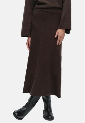 Brun stickad maxikjol med en åtsittande midja, avsmalnande silhuett och strukturerad tyg, kombinerad med svarta knähöga stövlar.