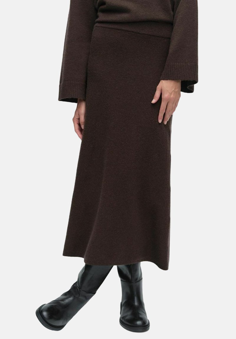 Ruskea neulepitsihame, jossa on istuva vyötärö, kapeneva siluetti ja teksturoitu kangas, yhdistettynä mustiin polven yli ulottuviin saappaisiin.