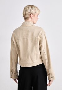 Bežna jeans jakna s skrajšanim dizajnom, klasičnim ovratnikom in zapenjanjem na manšetah. Ima gladko teksturo in subtilne šive.