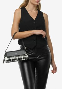 Zwart vesttop gecombineerd met strakke zwarte leren broeken. De tas heeft een rechthoekig ontwerp in zwart-wit houndstooth patroon, met een slanke schouderband.