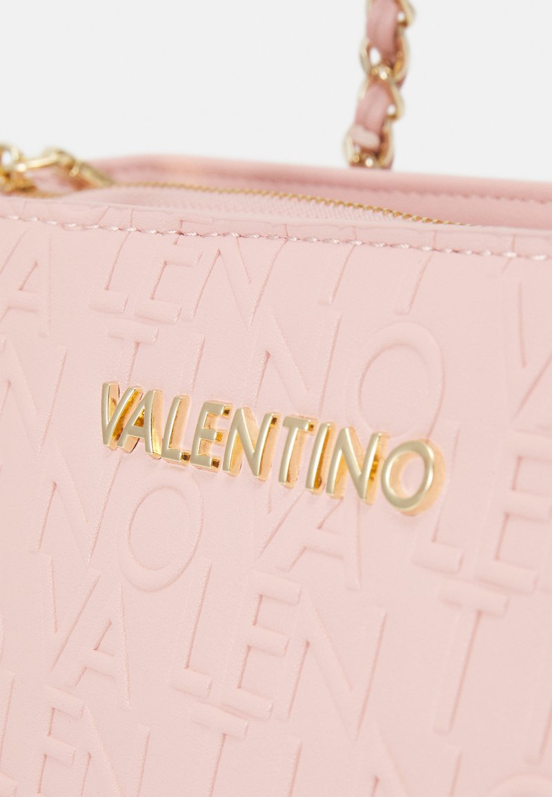 Sac à main en cuir rose avec un design de logo en relief, quincaillerie dorée et accent de chaîne sur la bandoulière. Fermeture éclair pour un accès sécurisé.