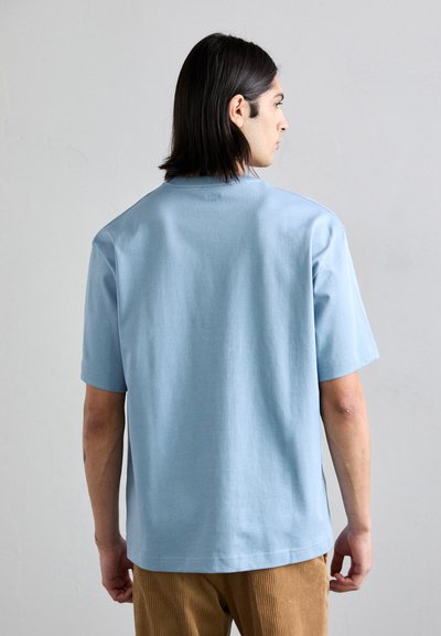 Camiseta de manga corta azul claro en una tela suave, con escote redondo y una sutil marca en la parte posterior.