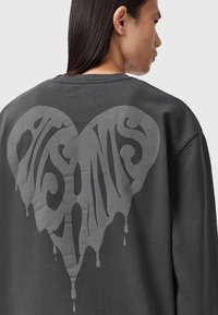 Grå sweatshirt med et stort drippende hjertegrafik i en mørkere nuance, lavet med en glat struktur på bomuldsstof.