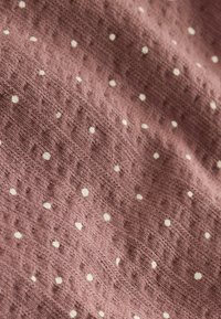 Tela suave color malva con pequeños lunares blancos, distribuidos uniformemente, y un patrón sutil de tejido texturizado.