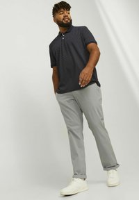 Navy polka dot polo shirt with a collar, paired with light gray trousers, and white sneakers. Casual fit with short sleeves and rolled cuffs.