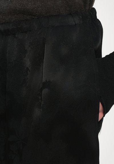 Black satin pants featuring a subtle floral pattern, elastic waistband, and side pockets; smooth texture with a glossy finish.