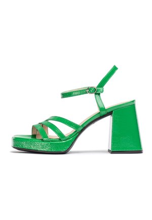 Sandalias de bloque de tacón de cuero sintético verde con tira en el tobillo, que presentan un diseño de tiras entrecruzadas y punta abierta. Textura brillante, forma moderna.
