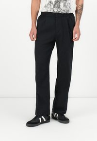 Pantalon noir à coupe décontractée, avec une taille �élastique et des plis devant. Associé à des baskets noires et une chemise blanche à motifs.