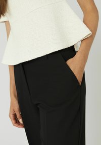 Haut peplum texturé blanc avec une couture de taille cachée, associé à un pantalon noir taillé avec des poches latérales et une finition lisse.