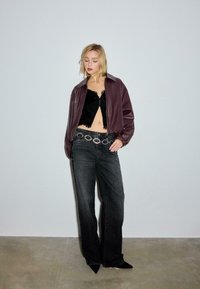 Bordeauxrød læderbomberjakke over en sort crop top i blonder. Sorte jeans med høj talje og et sølvfarvet bælte med cirkeldetalje. Spidse sorte sko.