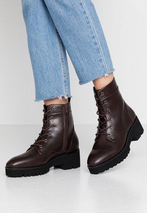 Donkerbruine leren enkellaarsjes met veters en een zijrits, gedragen met lichtblauwe cropped jeans op een witte vloer.