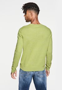 Jersey de punto verde con mangas largas y cuello redondo, con un acabado ligeramente texturizado. Combinado con jeans de mezclilla azules.