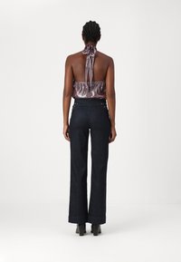 Top de cuello halter en burdeos metálico con la espalda al aire, combinado con pantalones acampanados de mezclilla oscura de cintura alta con accesorios plateados.