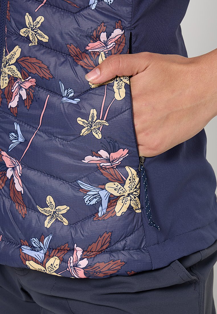 Chaleco acolchado de color azul marino con estampado floral en rosa, amarillo y azul. Cuenta con un bolsillo lateral y una tela texturizada con un diseño acolchado.