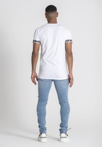Camiseta blanca con mangas cortas a cuadros, combinada con jeans ajustados de lavado claro. Los zapatos son blancos con acentos y texto en negro.