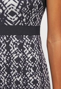 Vestido a rayas blanco y negro con un diseño geométrico. Acentuado con una cintura elástica negra. Textura de tela suave.