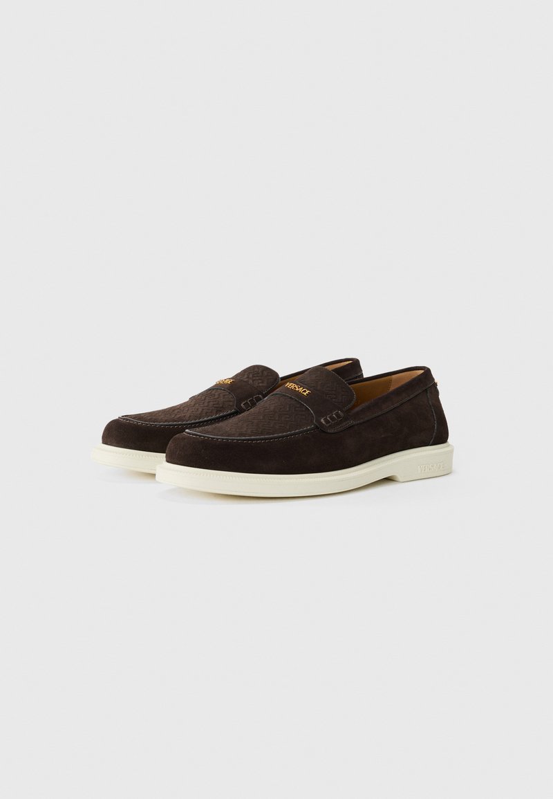 Dunkelbraune Wildleder-Loafer mit strukturiertem Stoff, cremefarbener Gummisohle und goldenen Logodetails auf der Vorderseite. Klassisches Slip-On-Design.