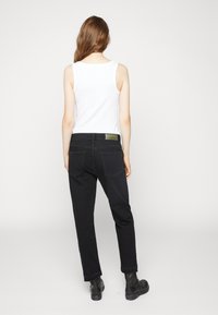 Pantalones de mezclilla negros de corte recto, con dobladillo ligeramente desgastado y dos bolsillos traseros. Combinados con una camiseta sin mangas blanca ajustada.