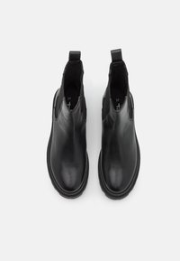 Bottes chevilles en cuir noir avec panneaux latéraux élastiques, orteils ronds et semelles rembourrées, présentant une texture lisse et un design minimaliste.