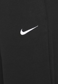Svarta träningsbyxor i texturerat tyg med en framträdande vit Nike-logga. Har en rak bendesign och elastiskt midjeband.