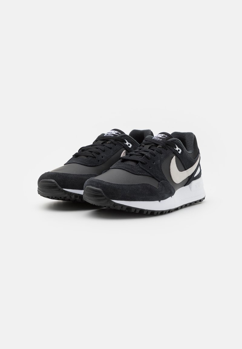 Schwarze Sportschuhe aus Wildleder und synthetischen Materialien, mit einem grauen Swoosh, schwarzen Schnürsenkeln und einer weißen Zwischensohle sowie einer strukturierten schwarzen Laufsohle.