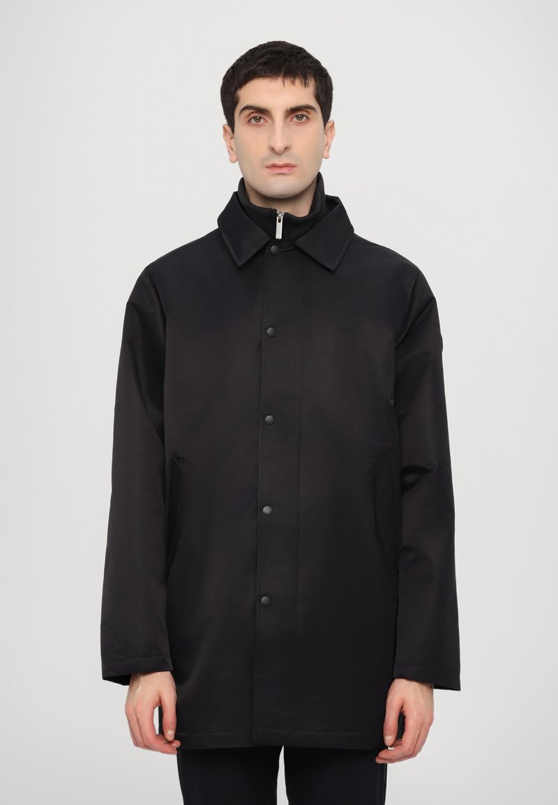 Black waterproof coat with a collar, front snap buttons, and side pockets, featuring a smooth texture and relaxed fit.