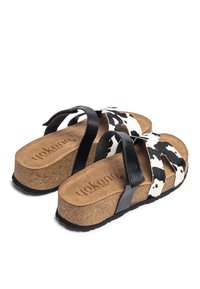 Cork platform sandals with black leather straps and cow print fabric. Features a textured footbed with branding, sturdy rubber sole.