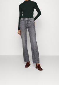 Jeans gris de tiro alto con corte recto, combinados con una blusa ajustada de manga larga verde oscuro y zapatos de tacón marrones.