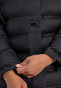 Chaqueta de abrigo negra con textura acolchada, que presenta un cierre de botones en la parte frontal y un detalle en el puño de la manga, resaltando su calidez y funcionalidad.