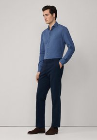 Blauses Langarmhemd mit Knöpfen, kombiniert mit dunkelblauen Hosen und braunen Schuhen. Glatte Stoff, taillierte Passform und minimale Designmerkmale.
