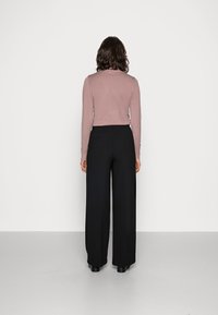 Langsleeve, strakke roze trui gecombineerd met hoge, wijde zwarte broek. Platte schoenen, eenvoudige textuur, minimalistisch ontwerp.