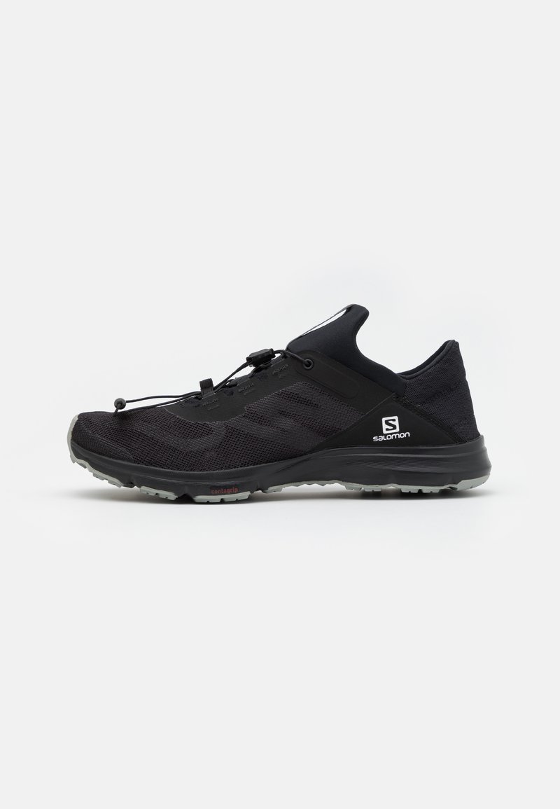 Chaussure de sport noire avec tige en mesh, un système de laçage rapide et une semelle texturée ; présente un logo sur le côté et à l'arrière.